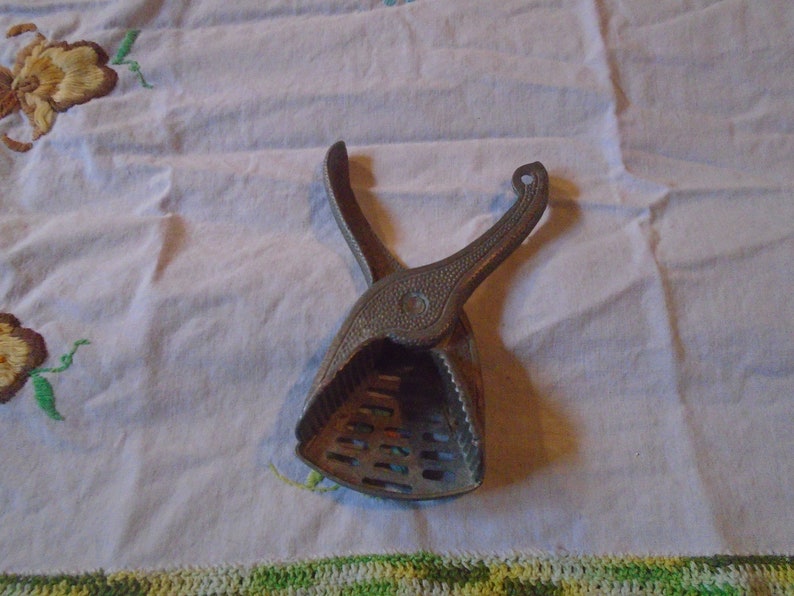May include: A vintage metal citrus juicer with a handle and a gridded base. The juicer is silver in color and has a worn, rustic look.