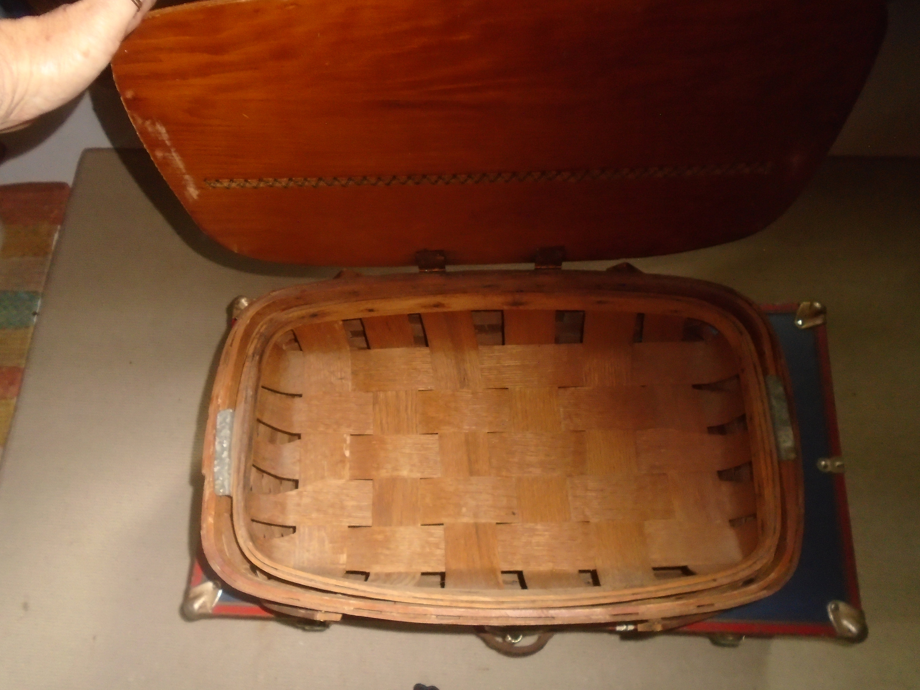 Puede incluir: Una cesta de picnic de madera con tapa abatible. La cesta est&aacute; hecha de madera trenzada y tiene un tinte marr&oacute;n. La tapa es de madera y tiene un tinte marr&oacute;n claro. La cesta est&aacute; vac&iacute;a.