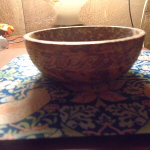 May include: A round, brown bowl with a textured surface. The bowl sits on a blue and white patterned mat with floral and bird designs. The bowl's interior is visible.