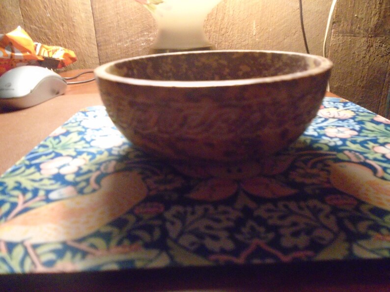 May include: A round, brown bowl with a textured surface. The bowl sits on a blue and white patterned mat with floral and bird designs. The bowl's interior is visible.