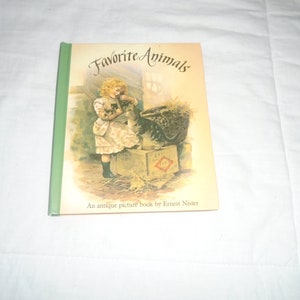 May include: A vintage children's book titled "Favorite Animals" with a green cover and an illustration of a young girl holding a kitten. The book is by Ernest Nister.