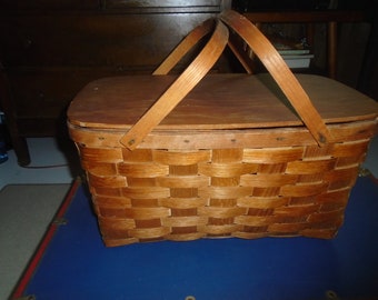 May include: A vintage wooden picnic basket with a woven design and a hinged lid. The basket has two wooden handles and is closed.