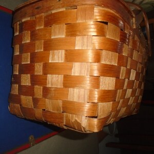 Puede incluir: Una cesta de mimbre tejida marr&oacute;n con un asa de madera.