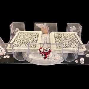 May include: A clear acrylic playing card and dice holder. The holder has slots for two decks of cards and several dice. A decorative heart with playing card symbols is in the center. The cards have a black and white floral design.