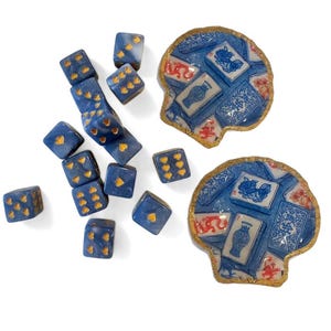 May include: A collection of blue dice with gold heart markings and two shell-shaped dishes. The dishes feature a blue and white design with gold trim. The dice are scattered, suggesting a game or decorative display.