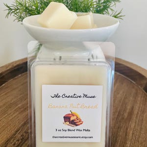 May include: A white ceramic wax warmer with a clear plastic container of soy wax melts. The container has a label that reads "Banana Nut Bread" and "3 oz Soy Blend Wax Melts". The warmer holds several wax cubes.