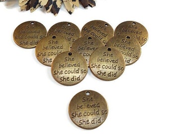 May include: A group of 10 round, bronze-colored metal charms with the text "She believed she could so she did" engraved on each charm.