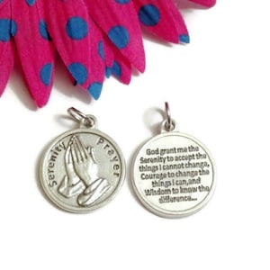 May include: Silver tone metal charm with the Serenity Prayer engraved on one side and a pair of praying hands on the other side.