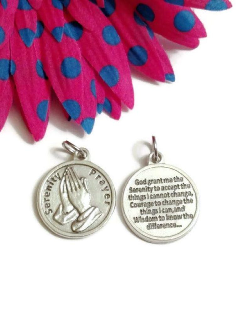 May include: Silver tone metal charm with the Serenity Prayer engraved on one side and a pair of praying hands on the other side.