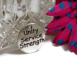 May include: A silver charm with the words "Unity Service Strength" engraved on it.