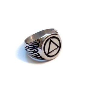May include: A silver ring with a black triangle inside a circle. The ring has a flame design on the band.
