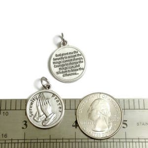 May include: Silver charm with a prayer for serenity. The charm is about 1 inch in diameter and features a praying hands design on one side and the Serenity Prayer on the other side.