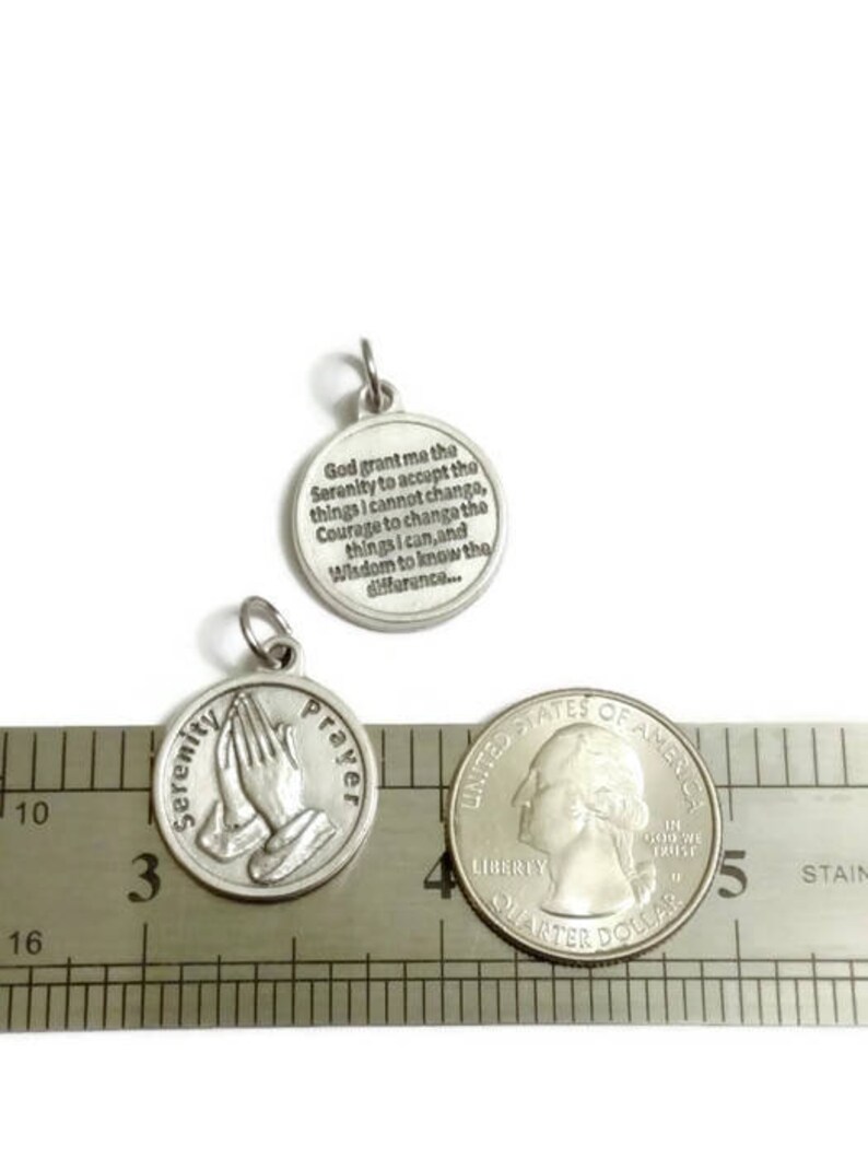 May include: Silver charm with a prayer for serenity. The charm is about 1 inch in diameter and features a praying hands design on one side and the Serenity Prayer on the other side.
