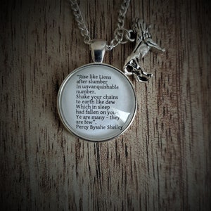 Könnte beinhalten: Eine silberne Halskette mit einem Glasanhänger, auf dem ein Zitat von Percy Bysshe Shelley steht: "Rise like Lions after slumber In unvanquishable number. Shake your chains to earth like dew Which in sleep had fallen on you- Ye are many - they are few".