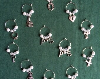 May include: Twelve silver wine glass charms with various designs, including a church, a horseshoe, a heart, a key, a cake, a bell, a dove, a ribbon, and the letters "PS".