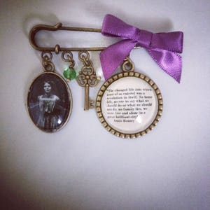 May include: A vintage-style brooch with a purple ribbon, a key charm, a glass cameo with a woman's portrait, and a round charm with a quote by Annie Kenney: "The changed life into which most of us entered was a revolution in itself. No home life, no one to say what we should do or what we should not do, no family ties, we were free and alone in a great brilliant city."