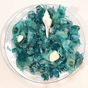 May include: A glass bowl filled with teal blue potpourri and white seashells. The potpourri is made of dried flowers and leaves.