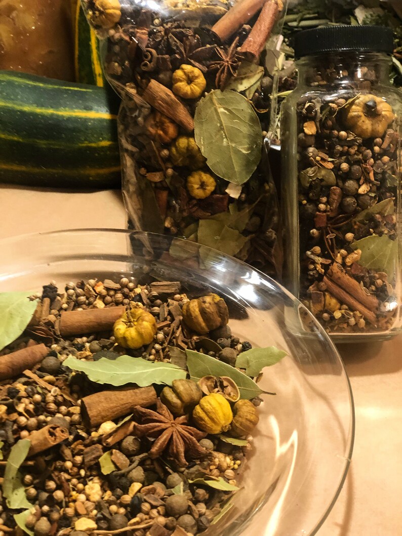 May include: A clear glass bowl and jars filled with a mix of spices, including cinnamon sticks, star anise, bay leaves, and small yellow gourds. The spices are arranged to create a visually appealing display, perfect for autumn decor or potpourri.