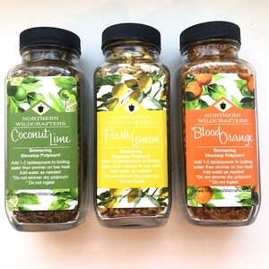 Könnte beinhalten: Drei Gläser mit köchelndem Topf-Potpourri mit schwarzen Deckeln. Die Gläser sind mit "Coconut Lime", "Fresh Lemon" und "Blood Orange" beschriftet. Jedes Etikett enthält Anweisungen und das Logo von Northern Wildcrafters.