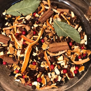 May include: A clear glass bowl containing a mixture of dried ingredients. The mix includes cinnamon sticks, orange peel, bay leaves, and red peppercorns. The ingredients are arranged in a visually appealing way.