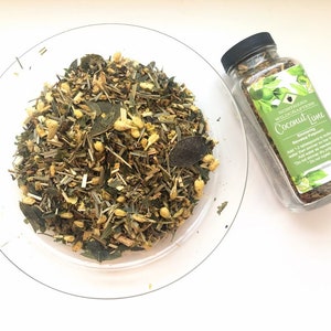 May include: A glass jar filled with loose leaf tea blend labeled "Coconut Lime" by Northern Wildcrafters. The tea blend is a mix of green, brown, and yellow herbs.  The jar is sitting on a white surface.
