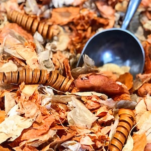 Peut inclure: Gros plan sur un tas de pétales de fleurs séchées orange et blanches et une louche en métal. Les pétales sont disposés de manière aléatoire et de différentes tailles. La louche est en métal et possède un manche.