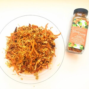 Könnte beinhalten: Ein Glas mit getrockneter Blutorangen-Schale mit einem Etikett, auf dem "Northern Wildcrafters Blood Orange Seasoning Supplement" steht. Das Glas steht auf einer weißen Oberfläche neben einem Teller mit getrockneter Orangenschale.