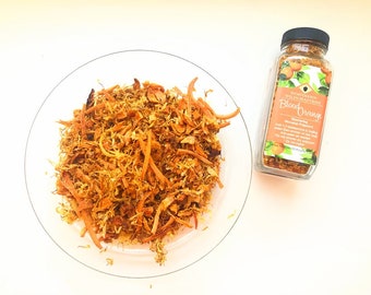 May include: A glass jar of dried blood orange zest with a label that reads "Northern Wildcrafters Blood Orange Seasoning Supplement". The jar is sitting on a white surface next to a plate of dried orange zest.