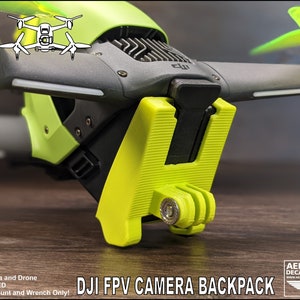 May include: A 3D printed green and black camera mount for a DJI FPV drone. The mount is designed to hold a GoPro camera and includes a GoPro mount. The text "DJI FPV CAMERA BACKPACK" is printed on the image.