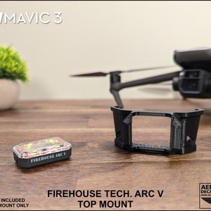 K&ouml;nnte beinhalten: Ein 3D-gedruckter Halter f&uuml;r eine DJI Mavic 3 Drohne. Der Halter ist schwarz und hat eine rechteckige &Ouml;ffnung in der Mitte. Der Text "FIREHOUSE TECH. ARC V TOP MOUNT" ist auf dem Halter aufgedruckt. Ein kleines, klares, rot-wei&szlig;es Stroboskoplicht ist ebenfalls abgebildet. Der Text "FIREHOUSE ARC V" ist auf dem Stroboskoplicht aufgedruckt.