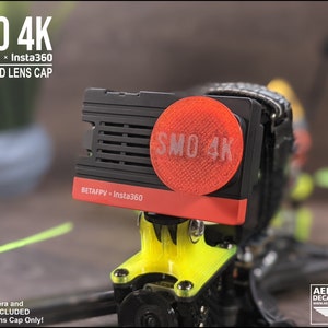 May include: A red and black 3D printed lens cap for a BetaFPV Insta360 SMO 4K camera. The lens cap has a red SMO 4K logo on it.
