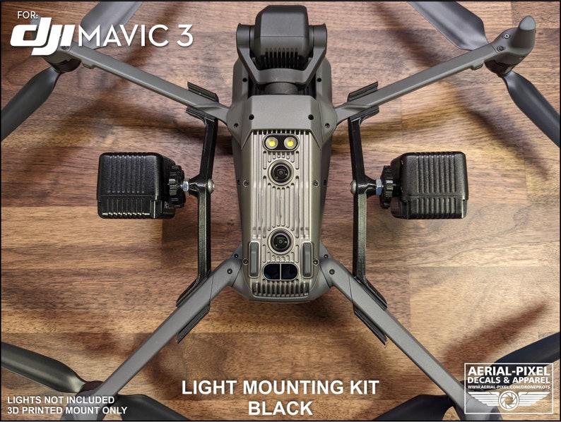 K&ouml;nnte beinhalten: Ein schwarzes Lichtmontage-Kit f&uuml;r eine DJI Mavic 3 Drohne. Das Kit enth&auml;lt zwei schwarze Lichthalterungen, die an den Armen der Drohne befestigt sind. Der Text "LIGHT MOUNTING KIT BLACK" ist sichtbar. Die Drohne ist grau mit schwarzen Propellern.