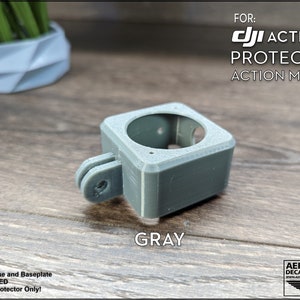 May include: Gray 3D printed protector for a DJI Action 2 camera. The protector has a GoPro-style mount.