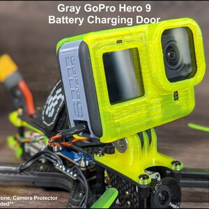 May include: Gray 3D printed GoPro Hero 9 battery charging door. The door is attached to a drone with a yellow and black frame. The text "GoPro Camera, Drone, Camera Protector and Cable Not Included" is visible at the bottom of the image.