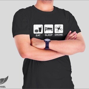 May include: A black t-shirt with a white graphic that says "Eat, Sleep, Drone". The graphic features icons for food, sleep, and a drone.