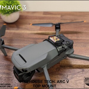 K&ouml;nnte beinhalten: Ein 3D-gedruckter Halter f&uuml;r eine DJI Mavic 3 Drohne. Der Halter ist schwarz und hat ein kleines, orangefarbenes Stroboskoplicht angebracht. Der Text "FIREHOUSE TECH. ARC V TOP MOUNT" ist auf dem Halter aufgedruckt. Der Text "STROBE NOT INCLUDED 3D PRINTED MOUNT ONLY" ist unter dem Halter aufgedruckt.