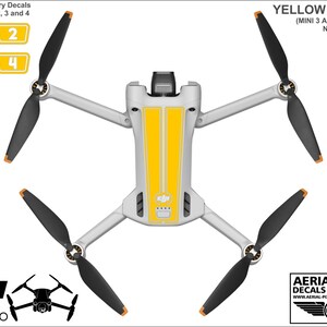 K&ouml;nnte beinhalten: Gelbe und wei&szlig;e Vinyl-Aufkleber f&uuml;r eine DJI Mini 3 Pro Drohne. Die Aufkleber beinhalten einen Satz von vier nummerierten Akku-Aufklebern und zwei lange Streifen f&uuml;r den Drohnenk&ouml;rper. Die Aufkleber werden separat von der Drohne und den Akkus verkauft.