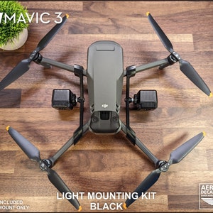 K&ouml;nnte beinhalten: Eine schwarze DJI Mavic 3 Drohne mit vier Propellern und zwei angebrachten Lichthalterungen. Der Text "LIGHT MOUNTING KIT BLACK" ist sichtbar. Das Bild enth&auml;lt auch den Text "FOR DJI MAVIC 3" und "LIGHTS NOT INCLUDED 3D PRINTED MOUNT ONLY".