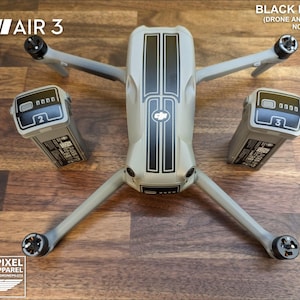 Op de afbeelding: Een drone met zwarte stickers en twee batterijen, met de tekst "FOR: DJI AIR 3" en "BLACK DECALS (DRONE AND BATTERIES NOT INCLUDED)". De drone is grijs met zwarte strepen en zwarte accenten. De batterijen zijn grijs met zwarte details.
