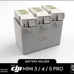 Op de afbeelding: Een grijze 3D-geprinte batterijhouder voor DJI Mini 3/4/5 Pro drones. De houder bevat drie witte batterijen met groene nummers 1, 2 en 3. De tekst "BATTERY HOLDER" en "DJI MINI 3/4/5 PRO" zijn zichtbaar.