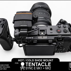 May include: A black camera accessory mount for a Tentacle Sync E MK1 and MK2, attached to a Sony camera body. The mount is a 3D printed black plastic piece featuring a hot/cold shoe design. The camera includes a Tamron lens and a side grip.