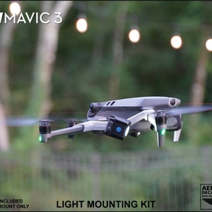K&ouml;nnte beinhalten: Eine graue DJI Mavic 3 Drohne mit sich drehenden Propellern und gr&uuml;nen Lichtern. Die Drohne hat einen Lichtmontagesatz angebracht. Der Text auf dem Bild lautet "FOR: DJI MAVIC 3" und "LIGHT MOUNTING KIT". Der Hintergrund ist verschwommen mit Bokeh-Lichtern.