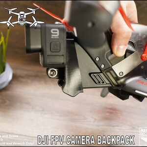 May include: A 3D printed mount for a GoPro camera, designed to fit a DJI FPV drone. The mount is black and has a clear plastic cover. The text "FA3RA4N" is printed on the drone arm. The text "DJI FPV CAMERA BACKPACK" is printed below the image.