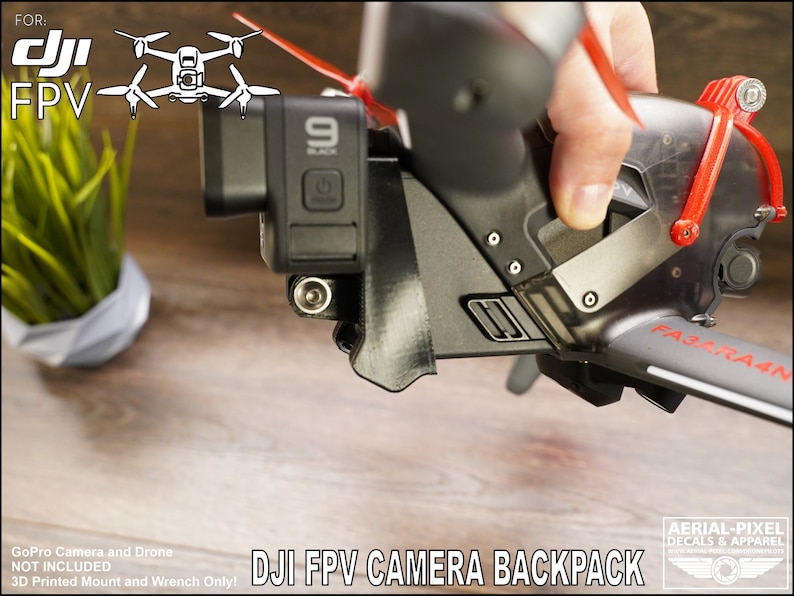 May include: A 3D printed mount for a GoPro camera, designed to fit a DJI FPV drone. The mount is black and has a clear plastic cover. The text "FA3RA4N" is printed on the drone arm. The text "DJI FPV CAMERA BACKPACK" is printed below the image.