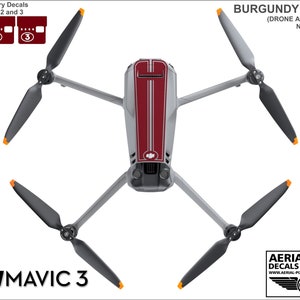 May include: Burgundy and gray vinyl decals for a DJI Mavic 3 drone. The decals include a red stripe down the center of the drone and two gray stripes on either side of the red stripe. The decals also include numbered decals for the drone's batteries.