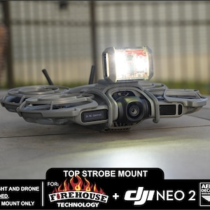 May include: A gray drone with a bright strobe light mounted on top. The drone has a camera and is labeled "DJI NEO 2". The text on the image reads "Top Strobe Mount" and "Firehouse Technology". The strobe light and drone are not included.
