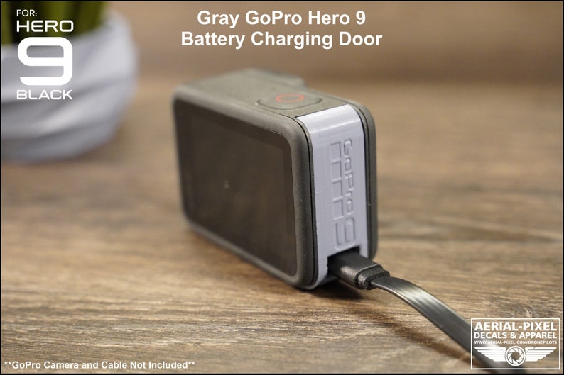 May include: Gray GoPro Hero 9 battery charging door. The door is attached to a gray GoPro Hero 9 camera. A black charging cable is plugged into the door. The text "GoPro Camera and Cable Not Included" is printed below the image.