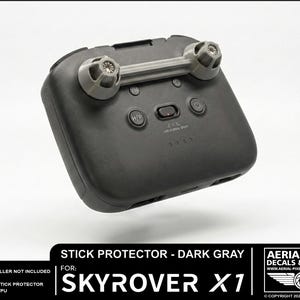 May include: Dark gray stick protector for Skyrover X1 remote controller. The protector has a rectangular shape with a gray bar and two gray knobs. The text "STICK PROTECTOR - DARK GRAY" and "SKYROVER X1" are visible.