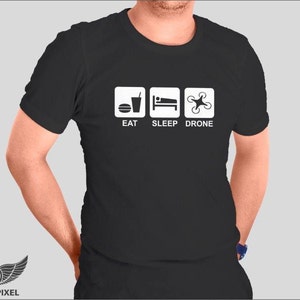 May include: Black t-shirt with white text and icons. The text reads "Eat Sleep Drone". The icons depict a drink, a bed, and a drone.