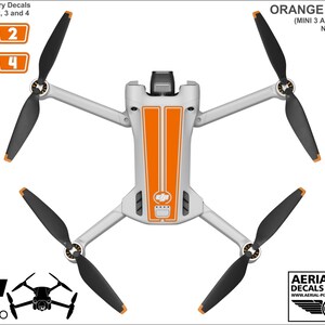 K&ouml;nnte beinhalten: Orangefarbene und wei&szlig;e Vinyl-Aufkleber f&uuml;r eine DJI Mini 3 Pro Drohne. Die Aufkleber beinhalten ein Streifen-Design auf dem Drohnenk&ouml;rper und nummerierte Aufkleber f&uuml;r die Batterien.